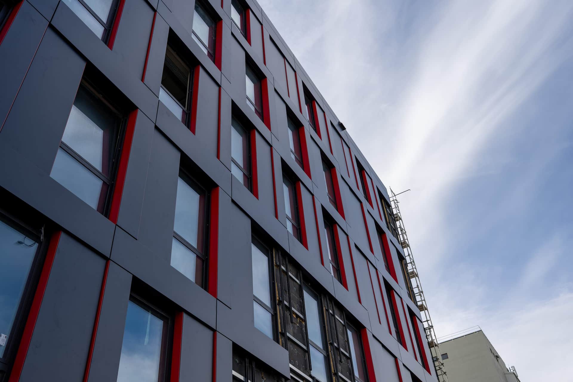 Geschwungene Metallfassade in Anthrazit mit roten Fensterlaibungen